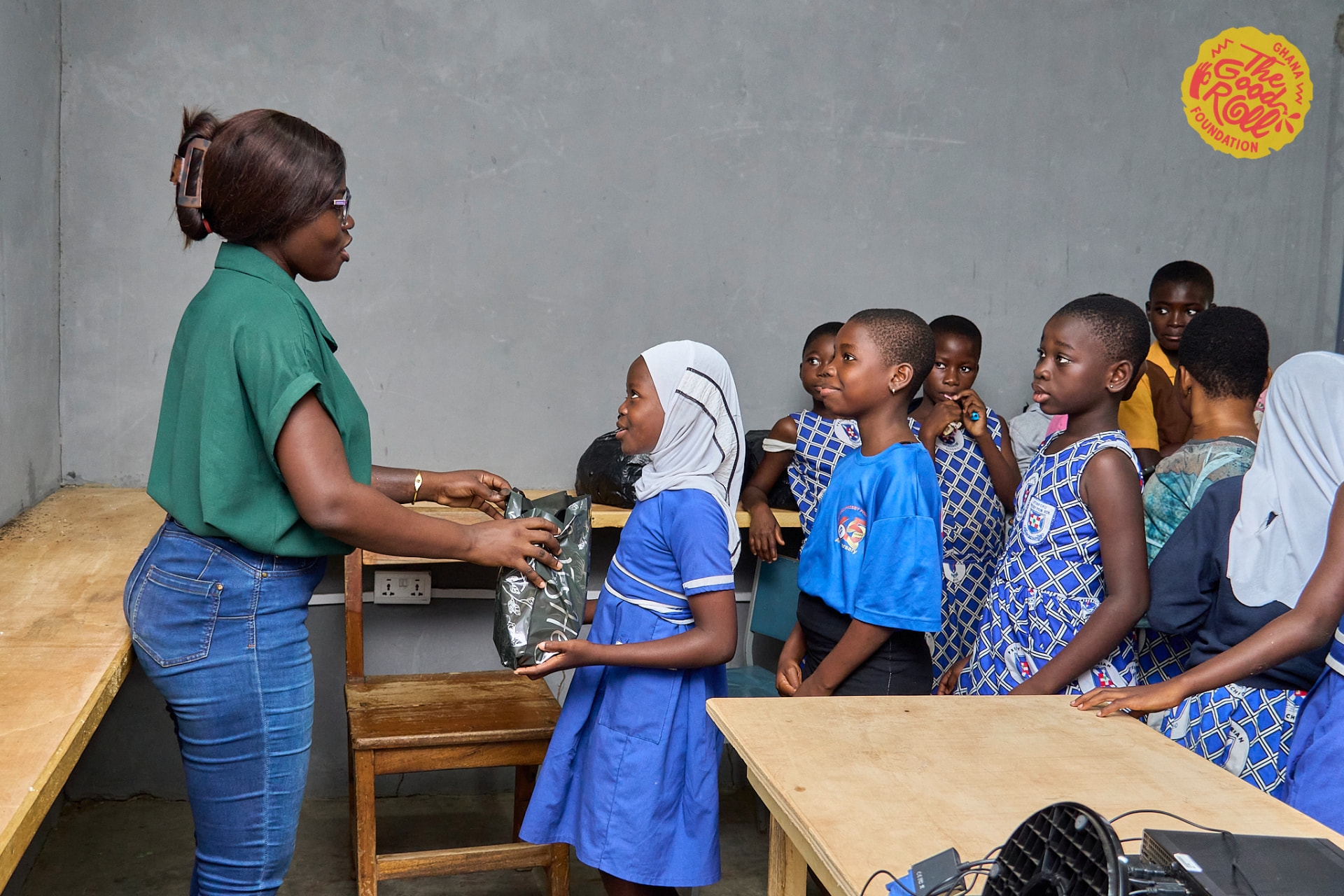 A team member hands a package to a schoolgirl in front of her classmates in a Ghanaian classroom