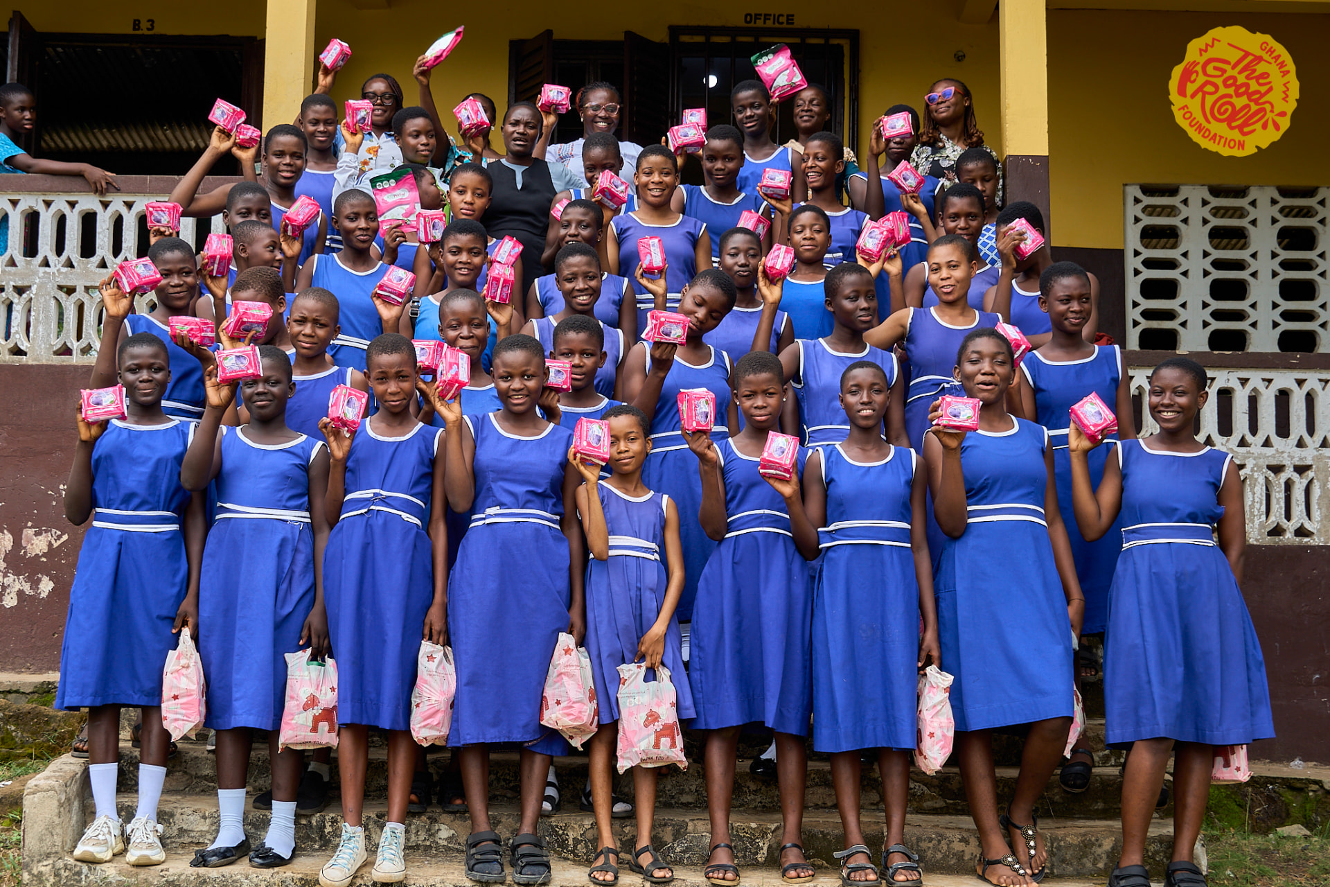 Groep schoolmeisjes poseert buiten het schoolgebouw met hun pakketten maandverband